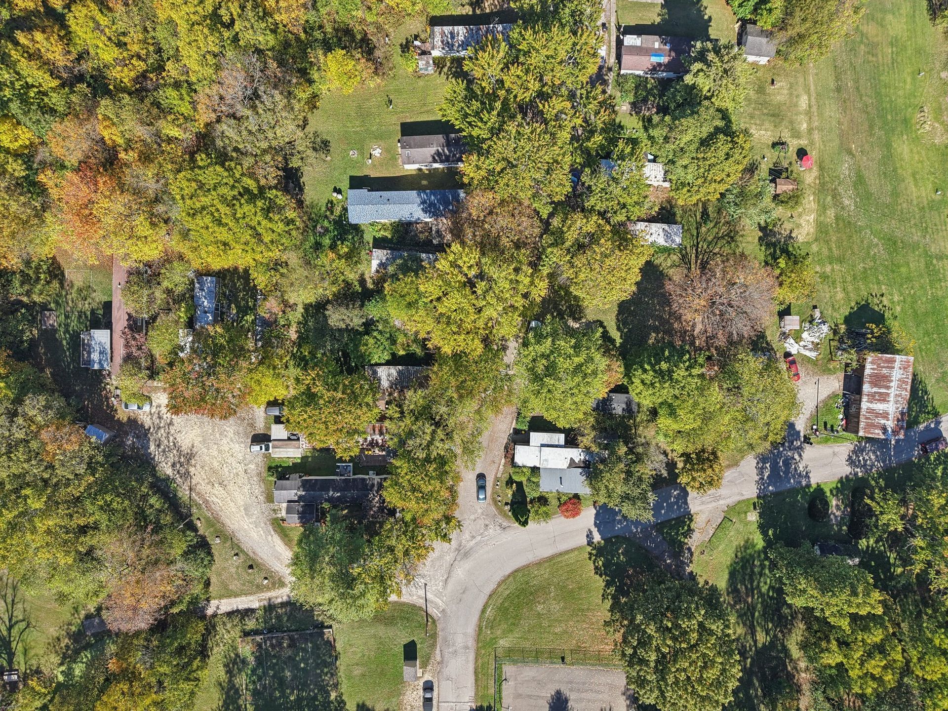 Aerial view of a small community with houses and trees. A curved road cuts through the center.