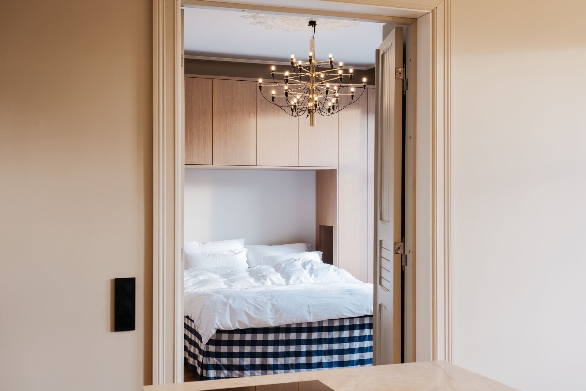 Soverom sett gjennom en åpen døråpning med seng, skap og lysekrone.