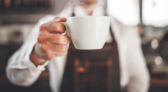 Barista presents cup of hot coffee at cafe