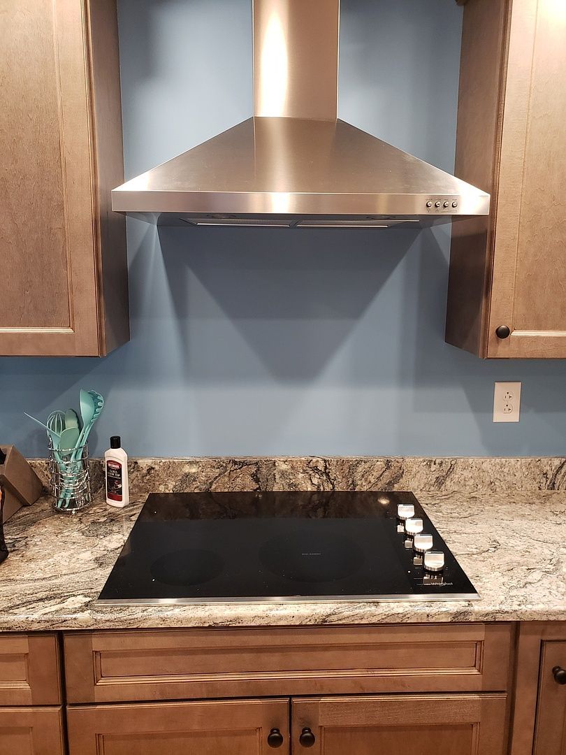 A kitchen with a stove top oven and a hood above it.