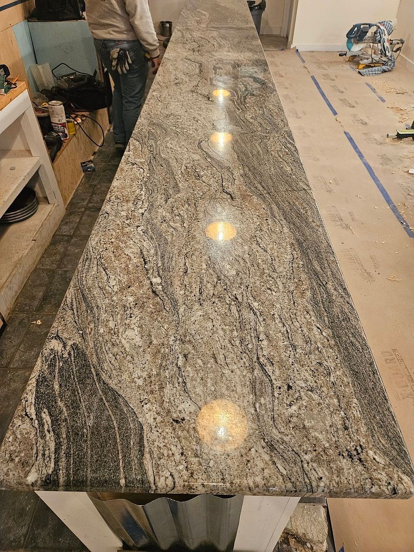 A man is standing next to a long granite counter top in a kitchen.