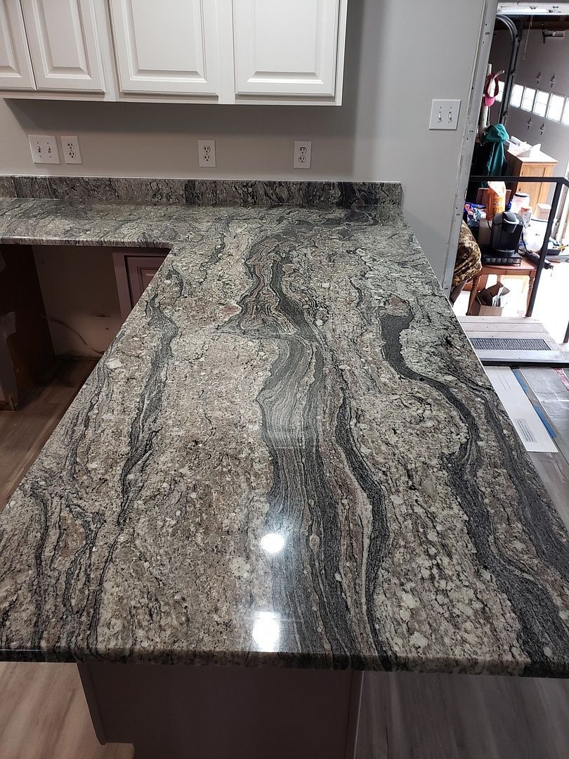 A man is standing next to a long granite counter top in a kitchen.