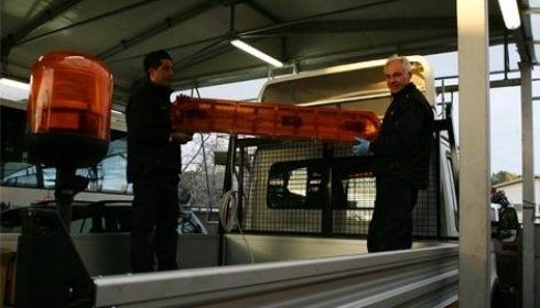 Due persone trasportano una barra luminosa arancione e la posizionano sul cassone di un camion.