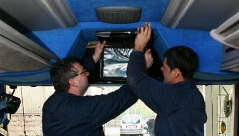 Due persone installano uno schermo all'interno di un veicolo, lavorando dall'alto. Interno blu con una luce esterna.