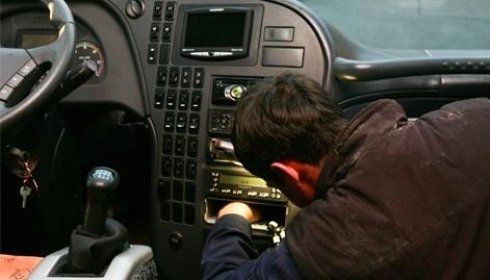 Persona che lavora sul cruscotto di un autobus o di un camion e allunga la mano verso la radio.