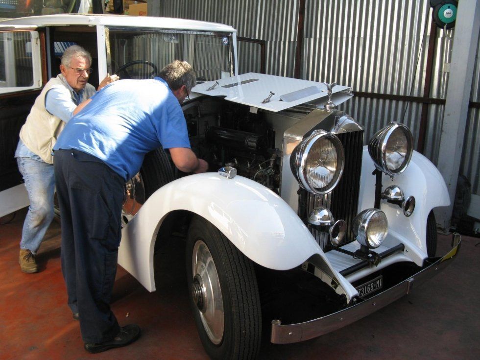 Due uomini lavorano sul motore di una classica auto bianca in un garage.