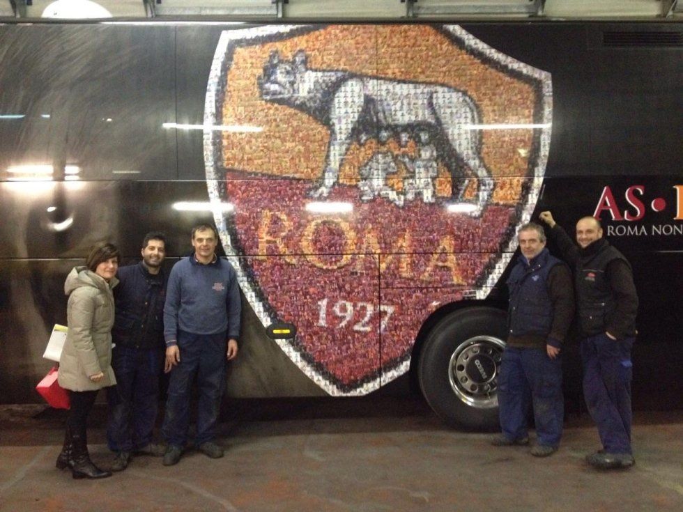 Persone in piedi accanto a un autobus nero con decorazioni della Roma