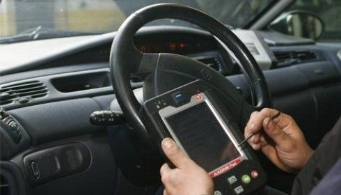 Persona che utilizza uno strumento diagnostico in un'auto per risolvere i problemi del veicolo. Si vede il volante nero.
