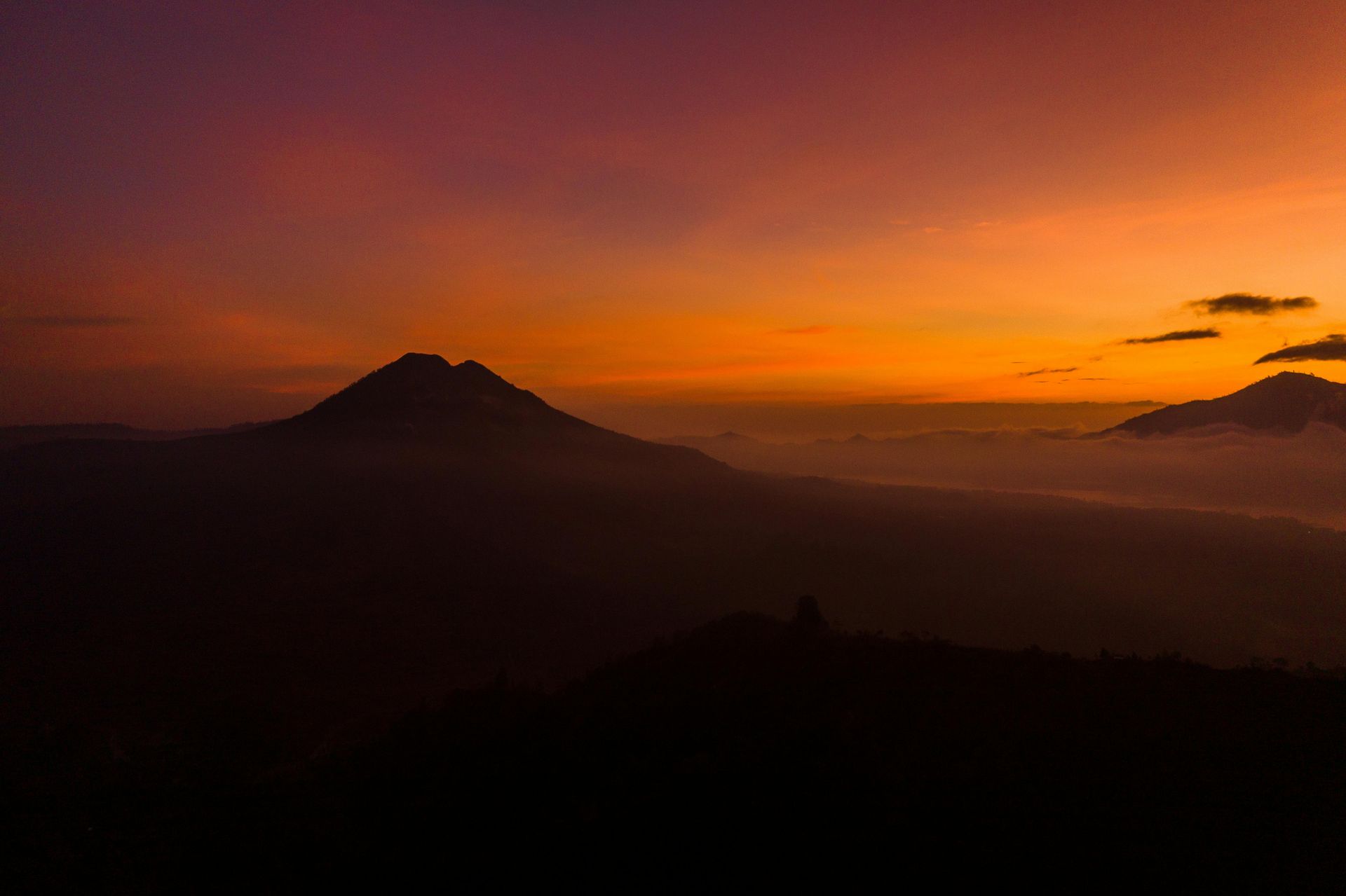 Sunset over silhouetted mountains, vibrant orange and purple sky.