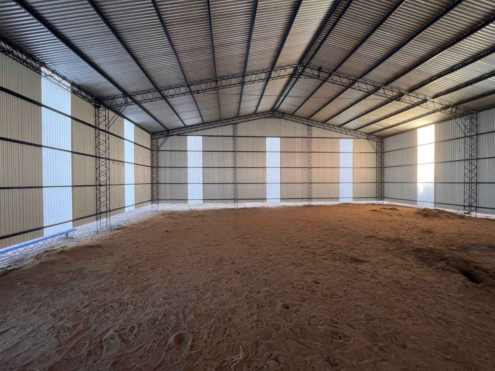 Interior de un cobertizo metálico con suelo de tierra. La luz del sol se filtra por los laterales.