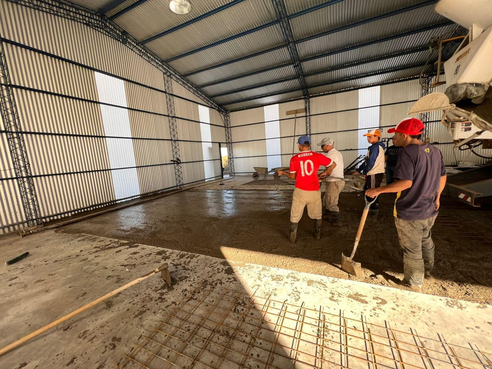 Obreros de la construcción vierten y nivelan el piso de hormigón en un gran edificio de metal.