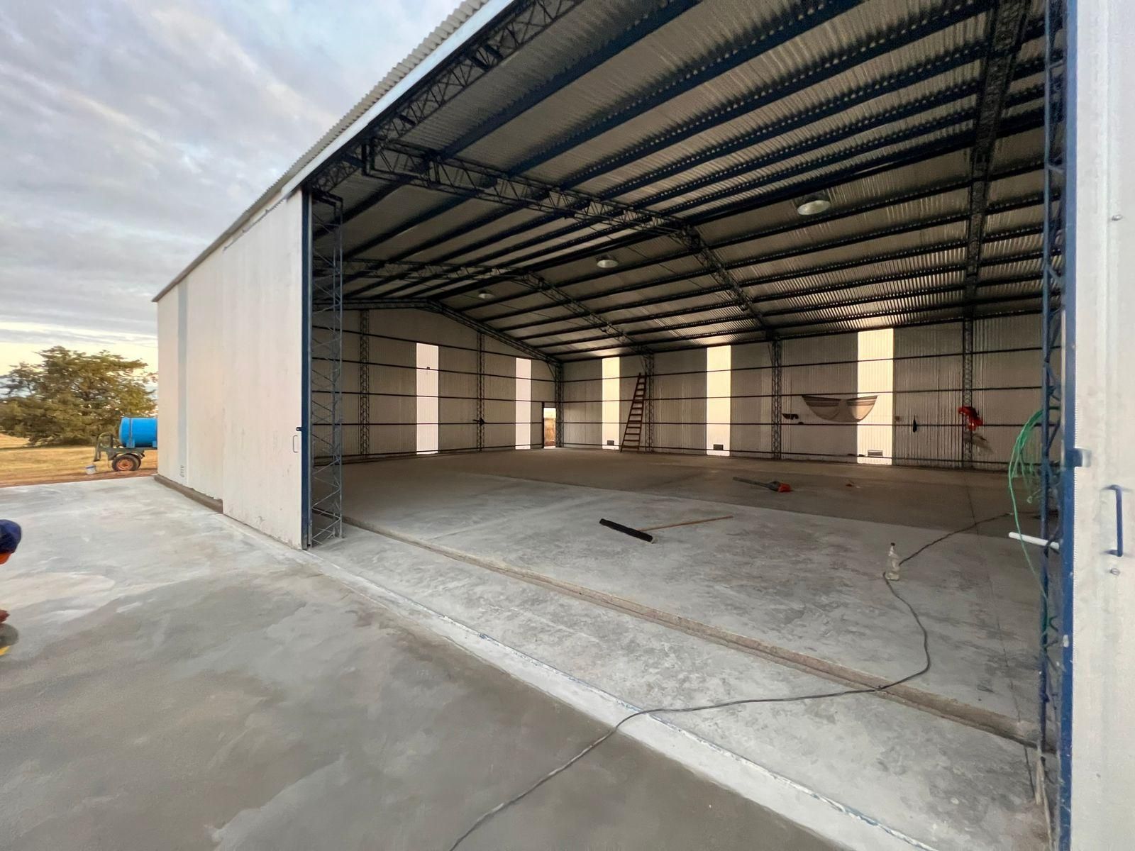 Gran edificio metálico vacío con puerta corrediza abierta sobre una losa de hormigón.