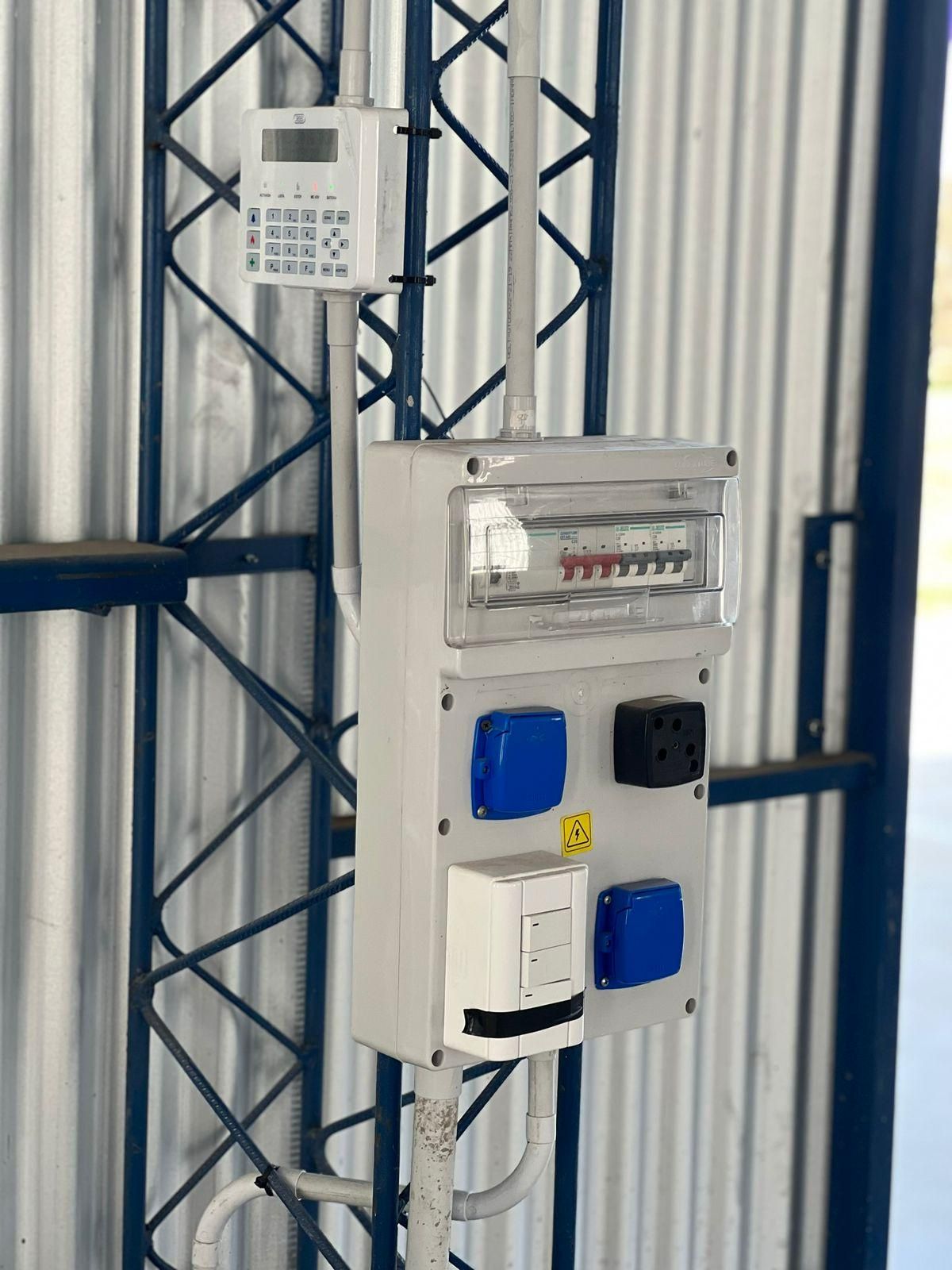 Cuadro eléctrico con tomas y temporizador montado sobre estructura metálica, con componentes de color azul, negro y blanco.