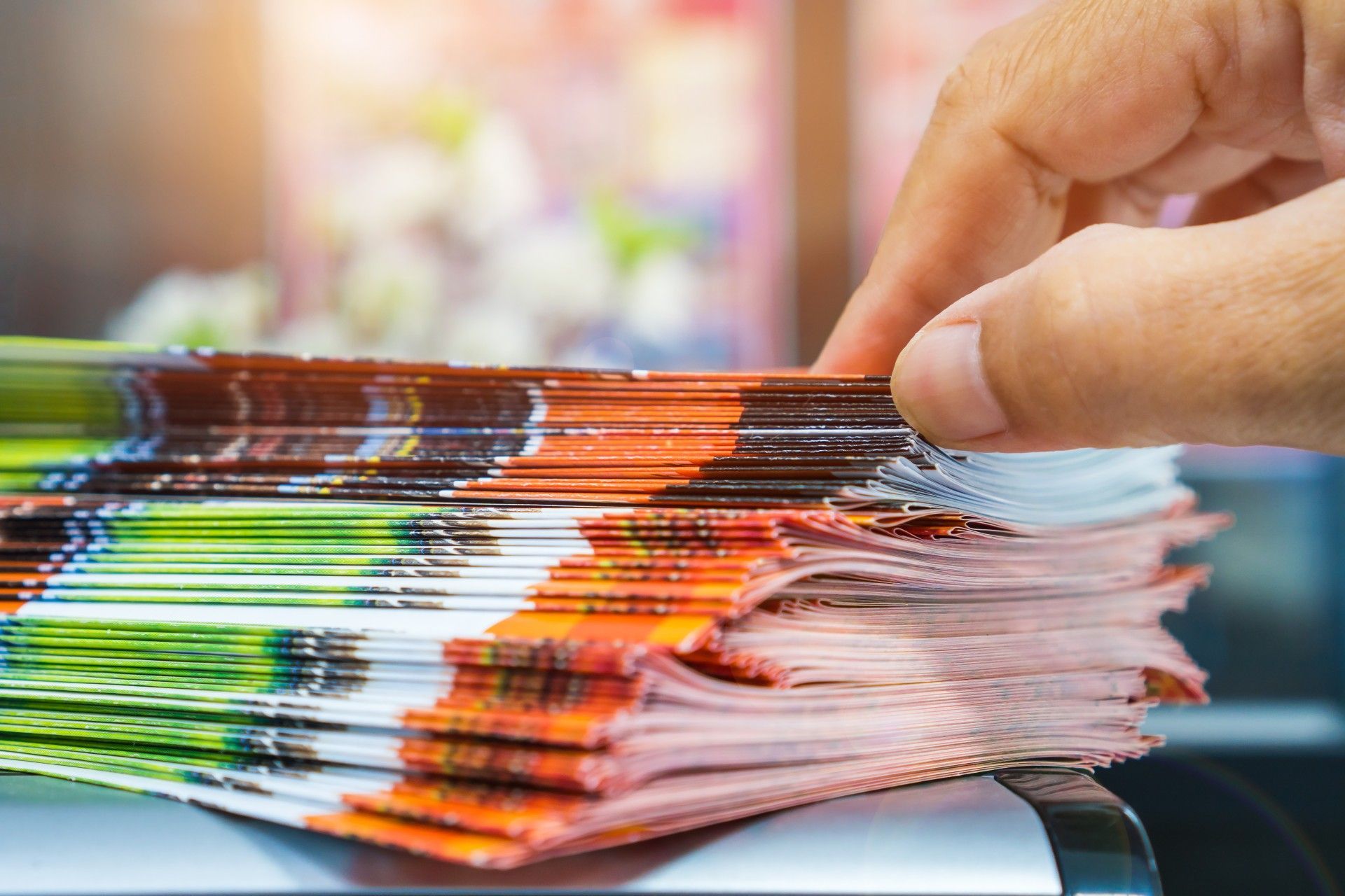 A person is holding a stack of magazines in their hand.