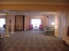 Spacious room with floral carpet, pillars, sofas, chairs, window with drapes.