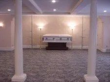 Funeral home interior with a casket centered beneath lamps, pillars in the foreground.