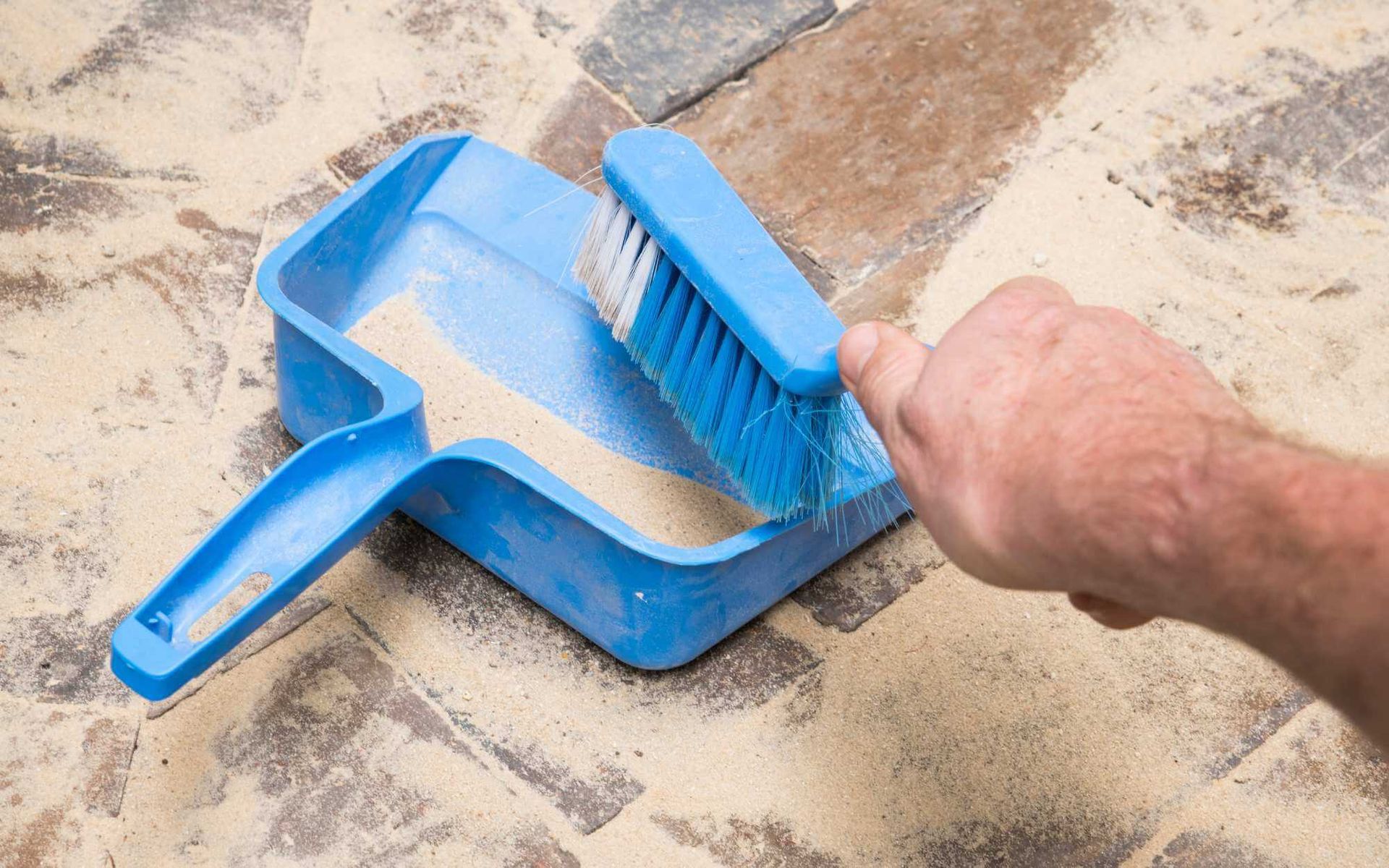 cleaning the paved surface with a handheld dustpan and broom