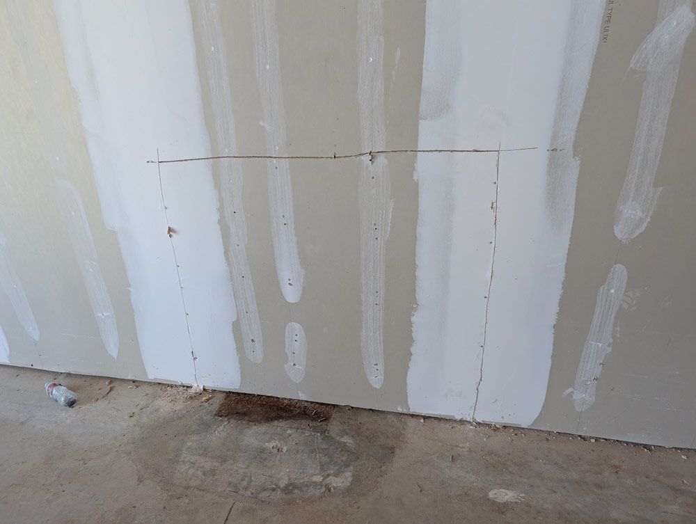 A rectangular section is marked in pencil on a gray, unfinished drywall wall near the floor of a construction site.