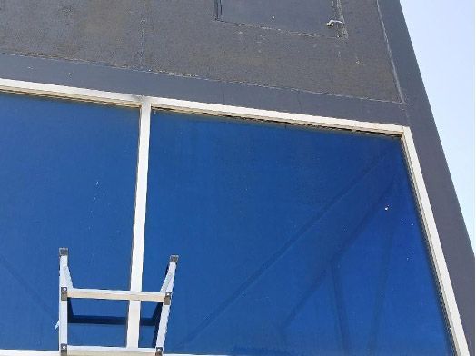A silver metal ladder propped against the white framing of a large, blue-tinted exterior window on a dark building.