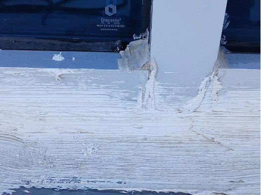 A close-up of a white painted wooden surface with peeling paint and sealant around a vertical post.