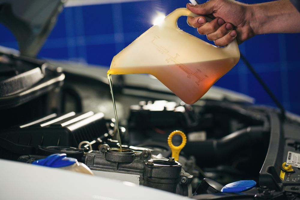 A Man is Putting a Yellow Oil Into a Car Engine — Mid Coast Bearing Centre in Wauchope, NSW
