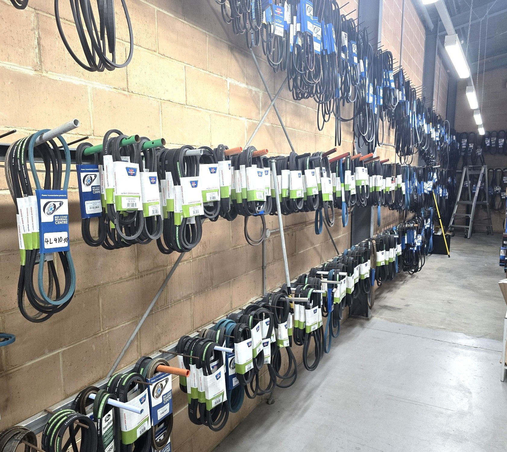 Rows of automotive belts hanging on a brick wall in a store, with fluorescent lighting.