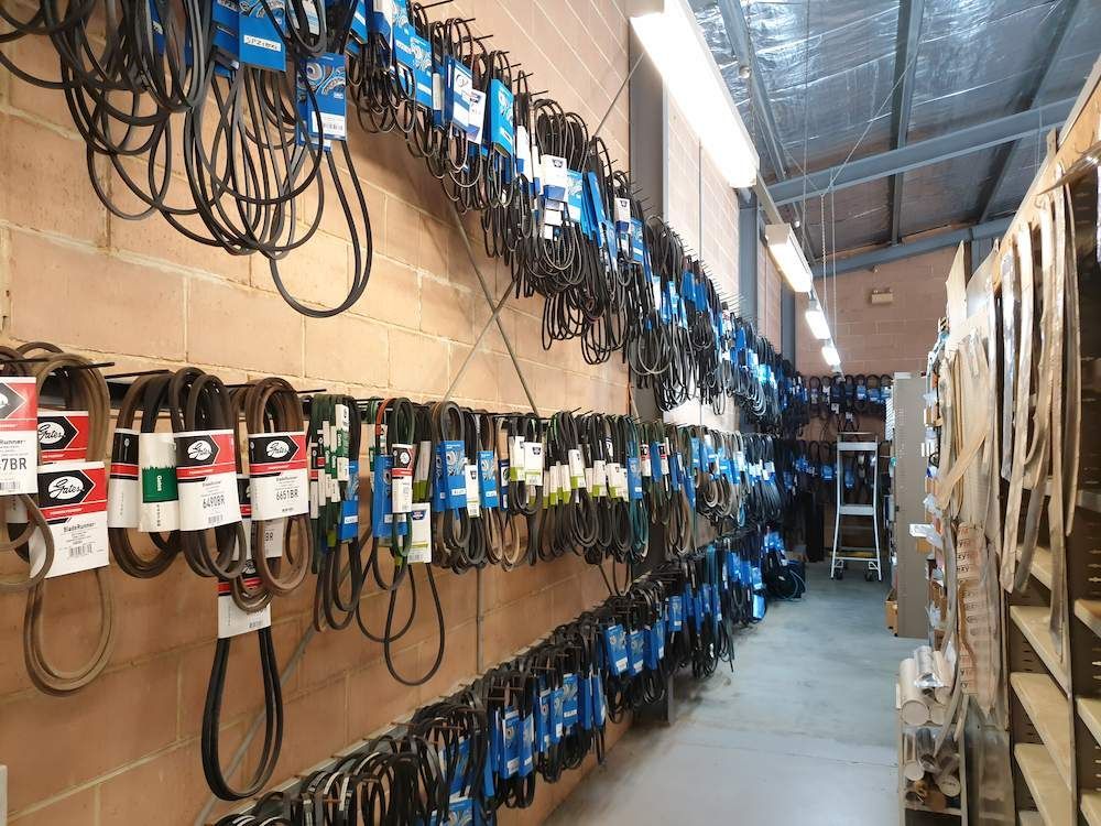 Belts of various types and sizes displayed for sale on a brick wall in a store.— Mid Coast Bearing Centre in Kempsey, NSW