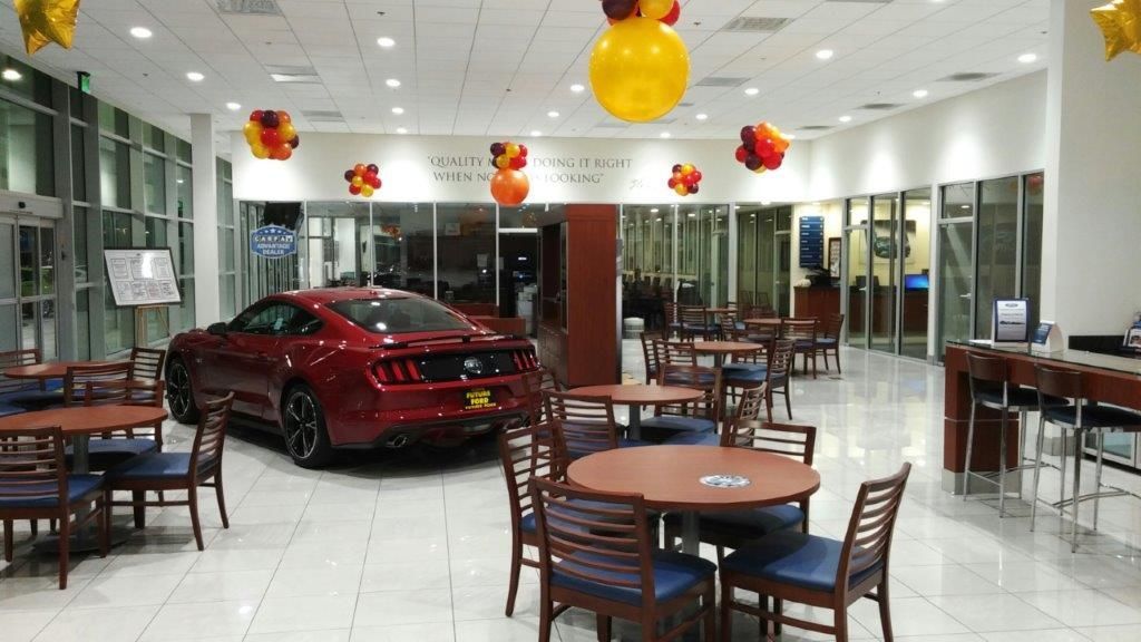 A red mustang is parked in a showroom with tables and chairs