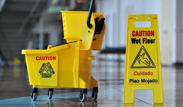 A yellow mop bucket is next to a caution wet floor sign