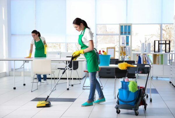 Two women are cleaning the floor of an office.