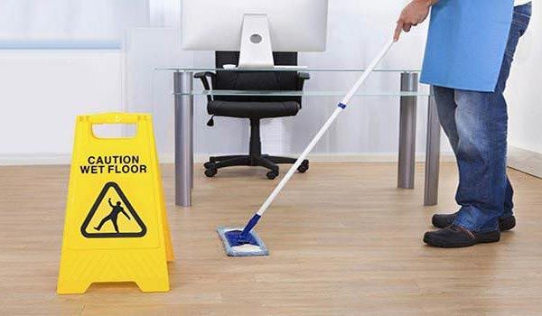 A man is mopping the floor next to a caution wet floor sign.