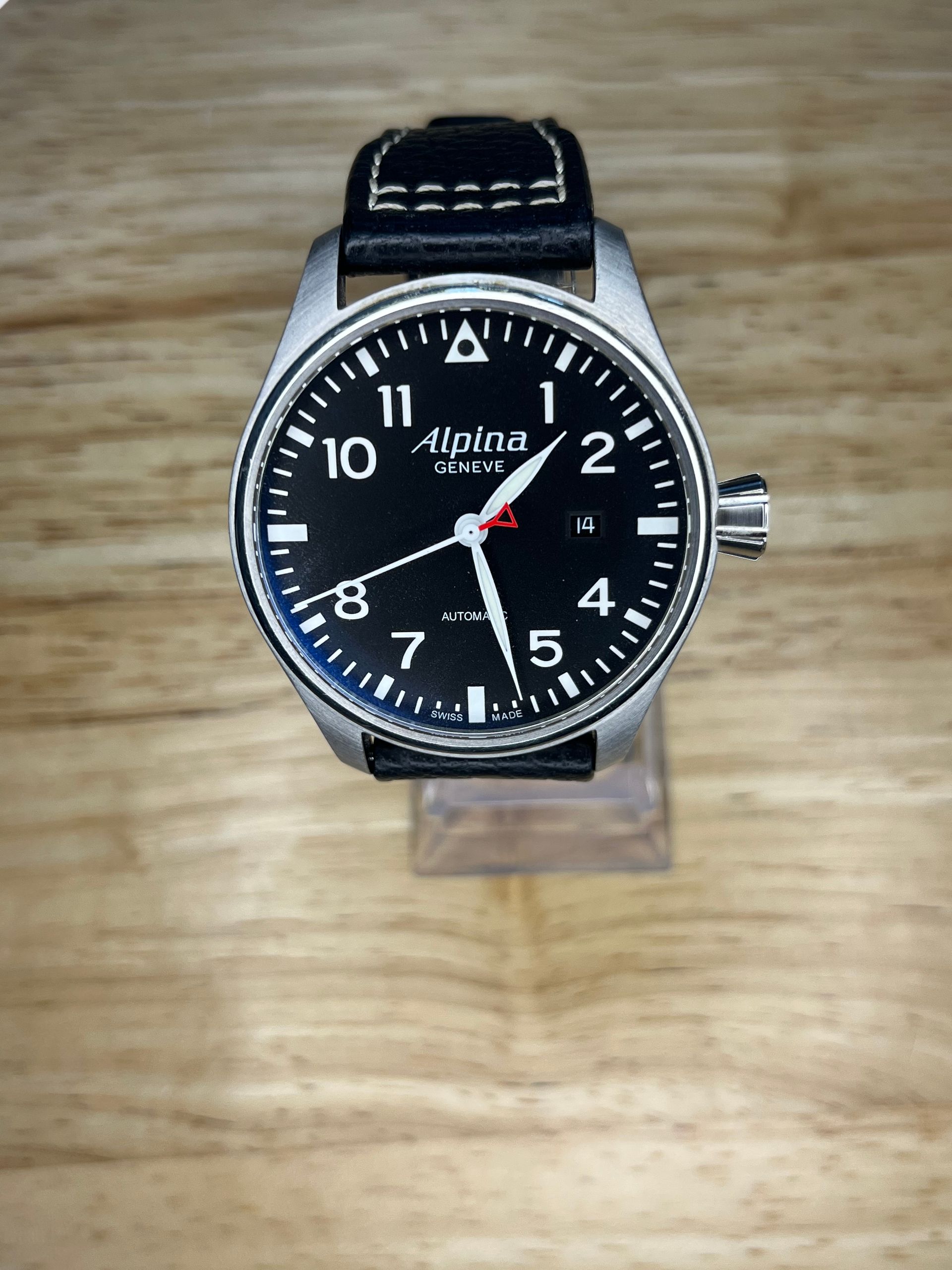 Silver watch with a black face, white numerals, and a leather band.