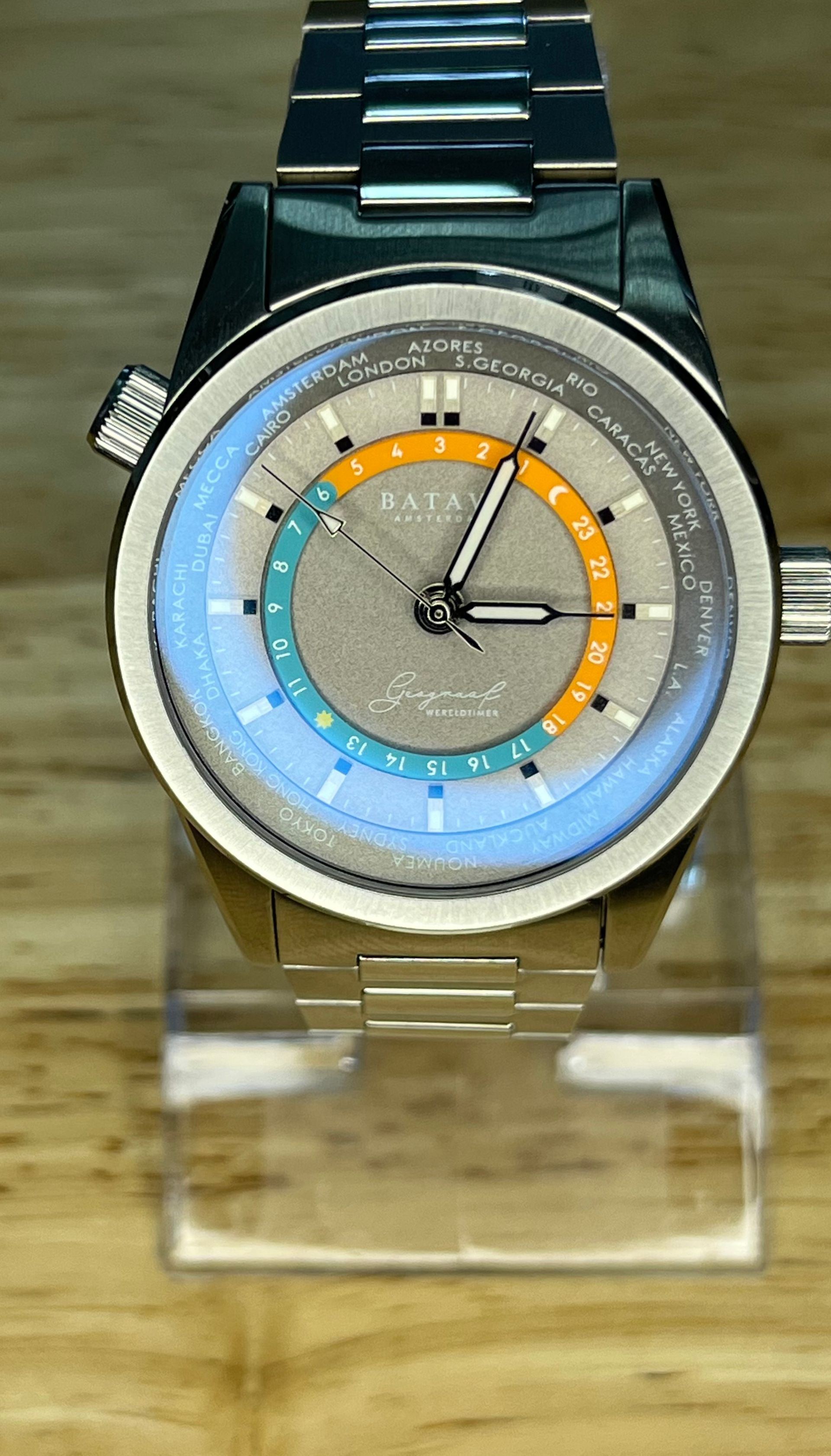 Silver wristwatch with a textured gray dial, orange and teal accents, and a world time indicator.