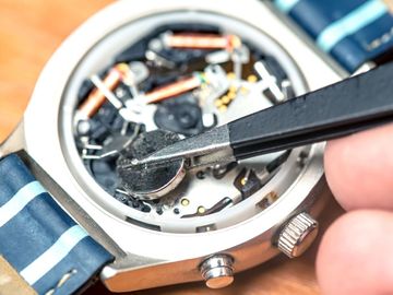 A person is fixing a watch with tweezers.