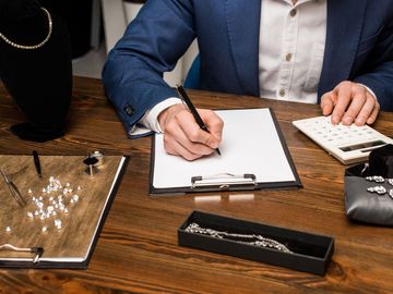 A man is writing on a clipboard while using a calculator.