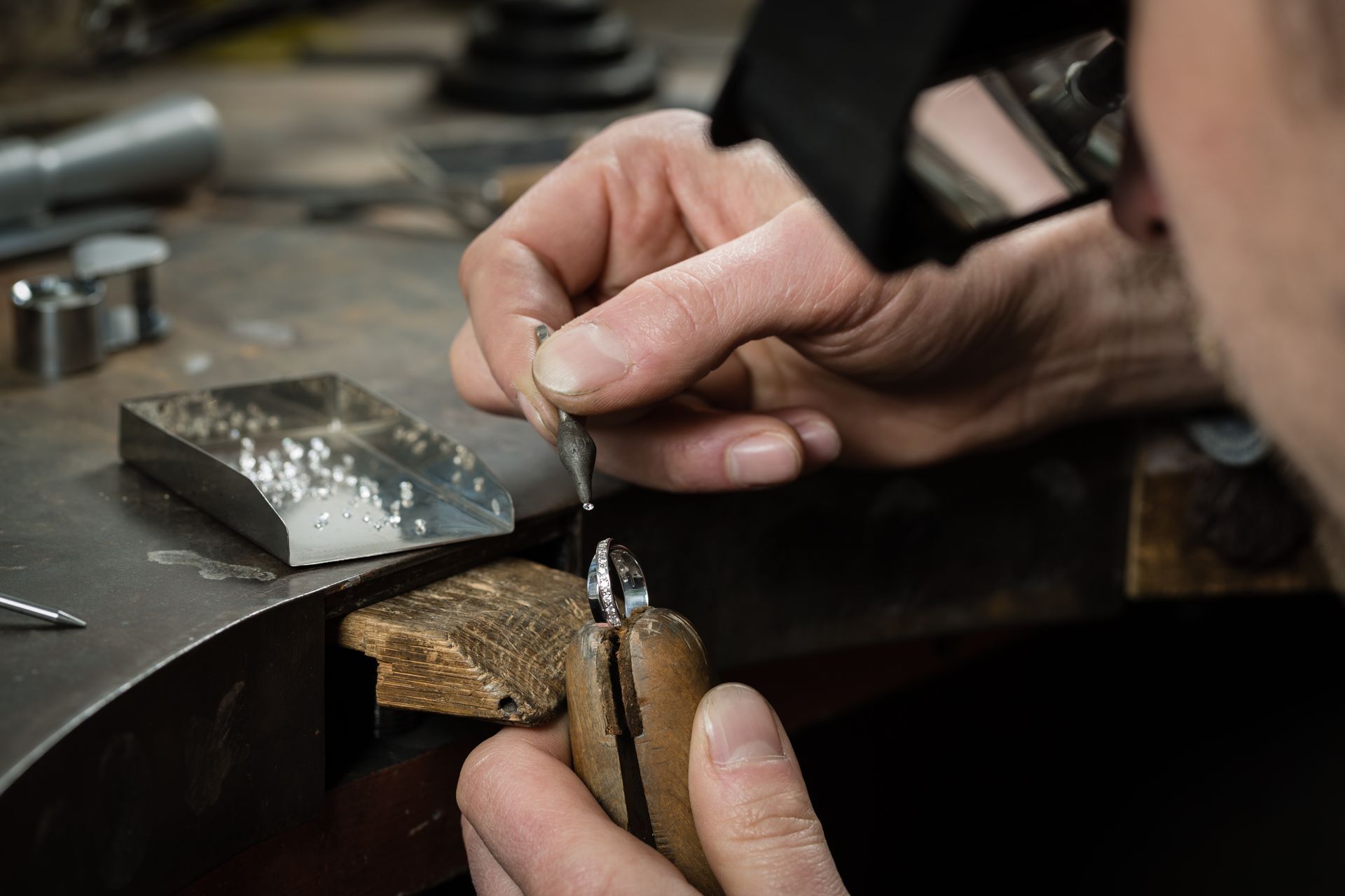 Jeweler working with small tools, shaping metal on a workbench, close-up.