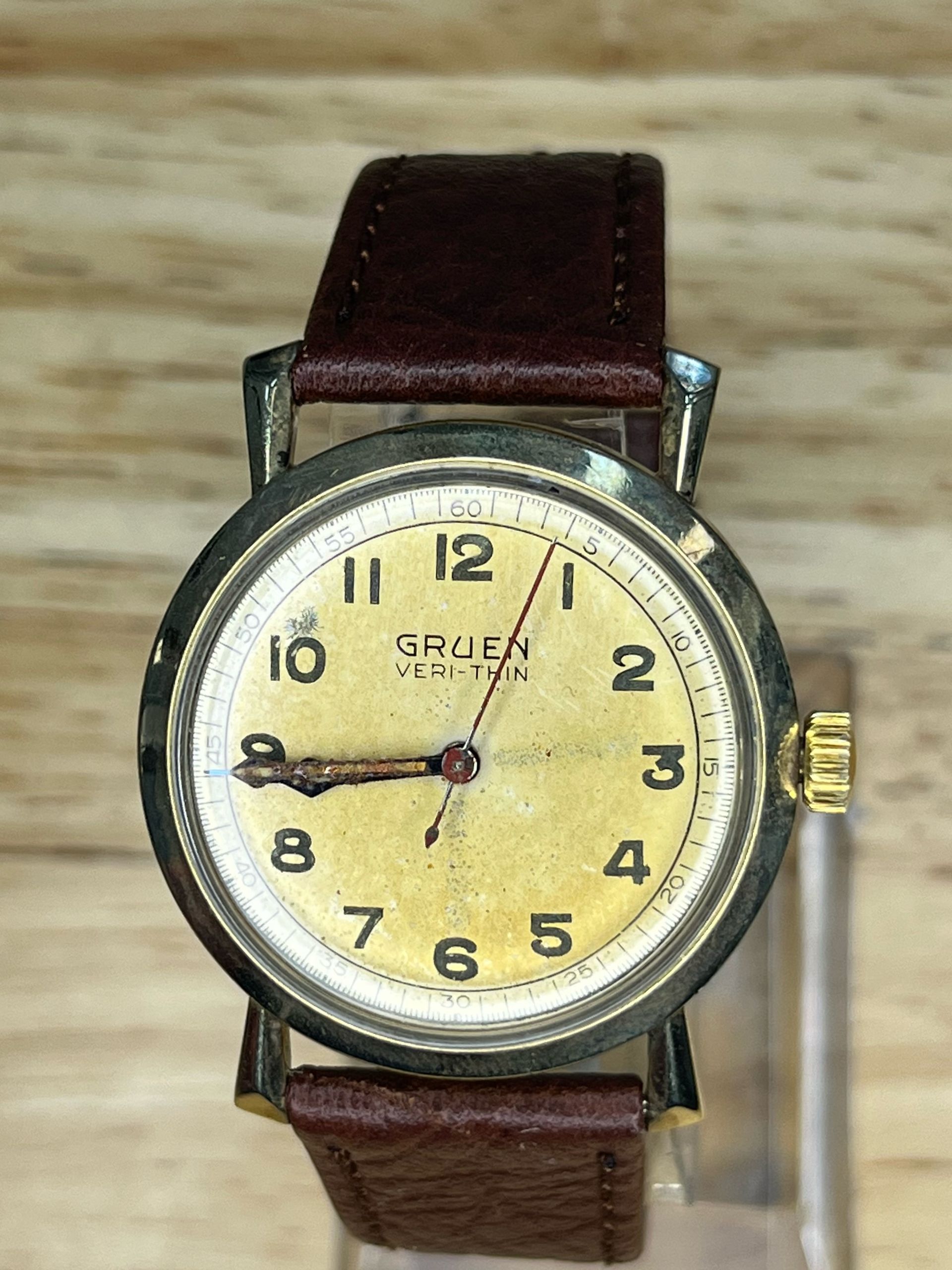 Gold-toned vintage Gruen wristwatch with brown leather strap on a wooden surface.