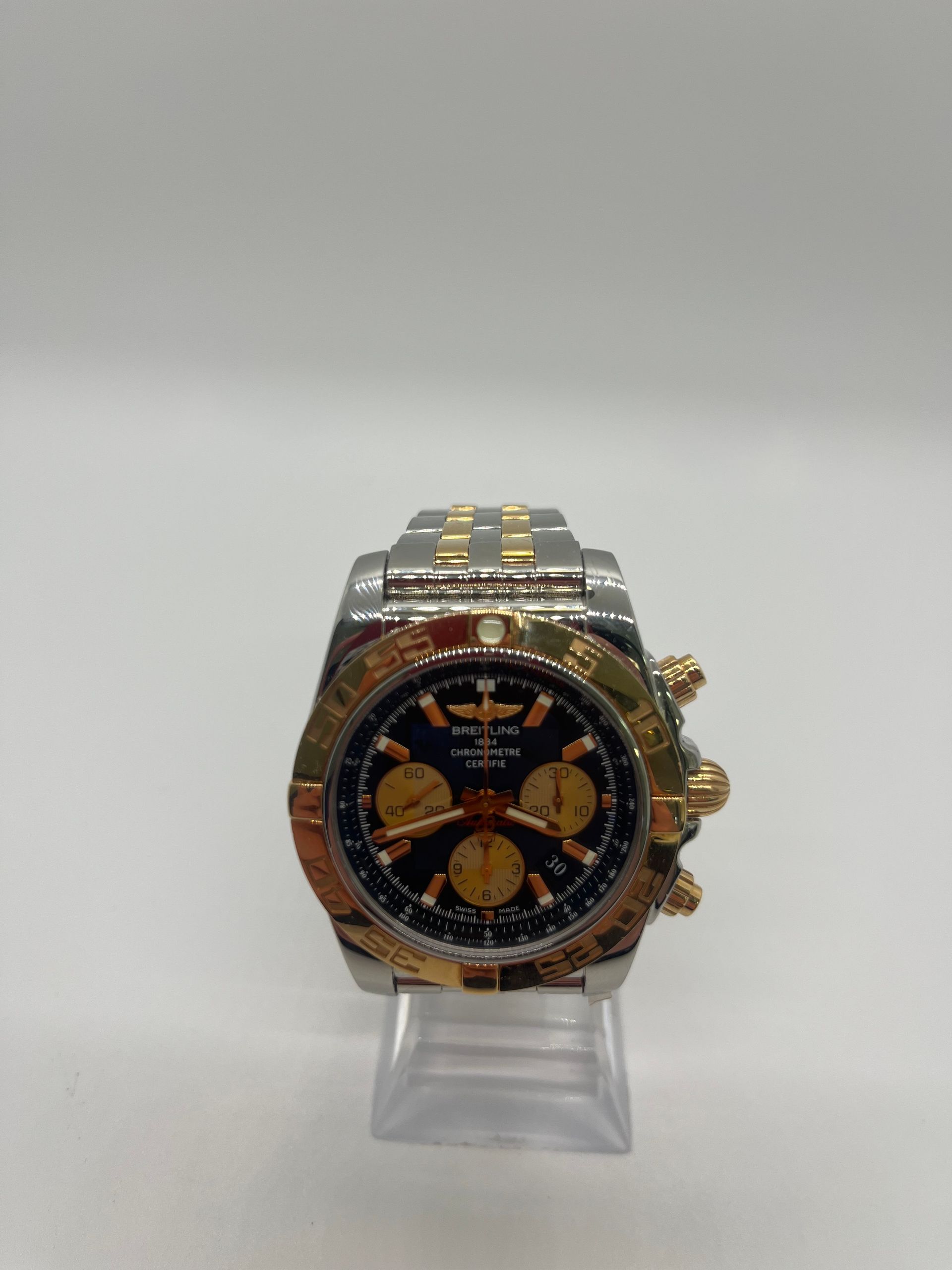 A Breitling watch with a black face and gold accents on a clear display stand.