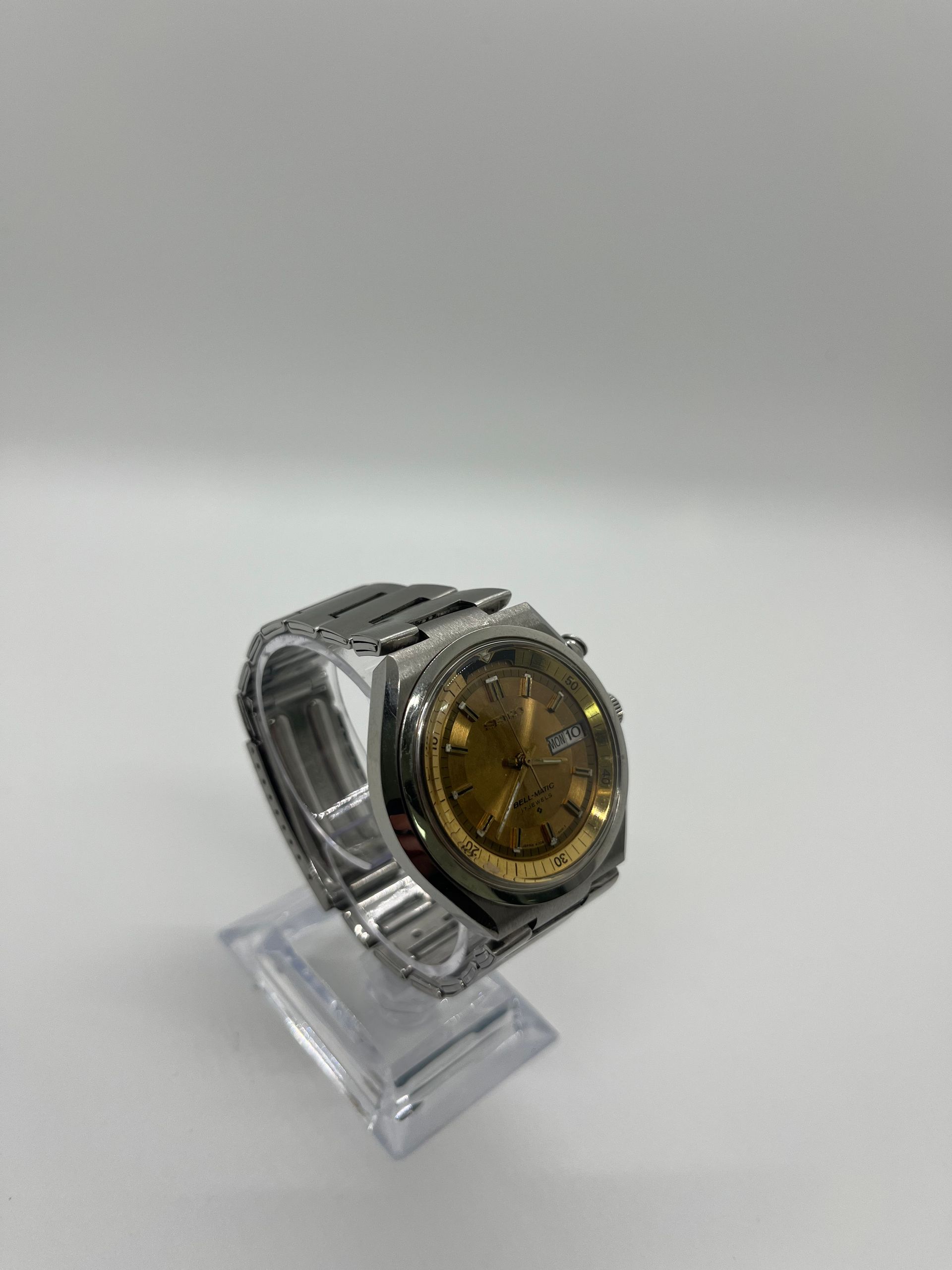 Silver wristwatch with gold face, on clear display stand.