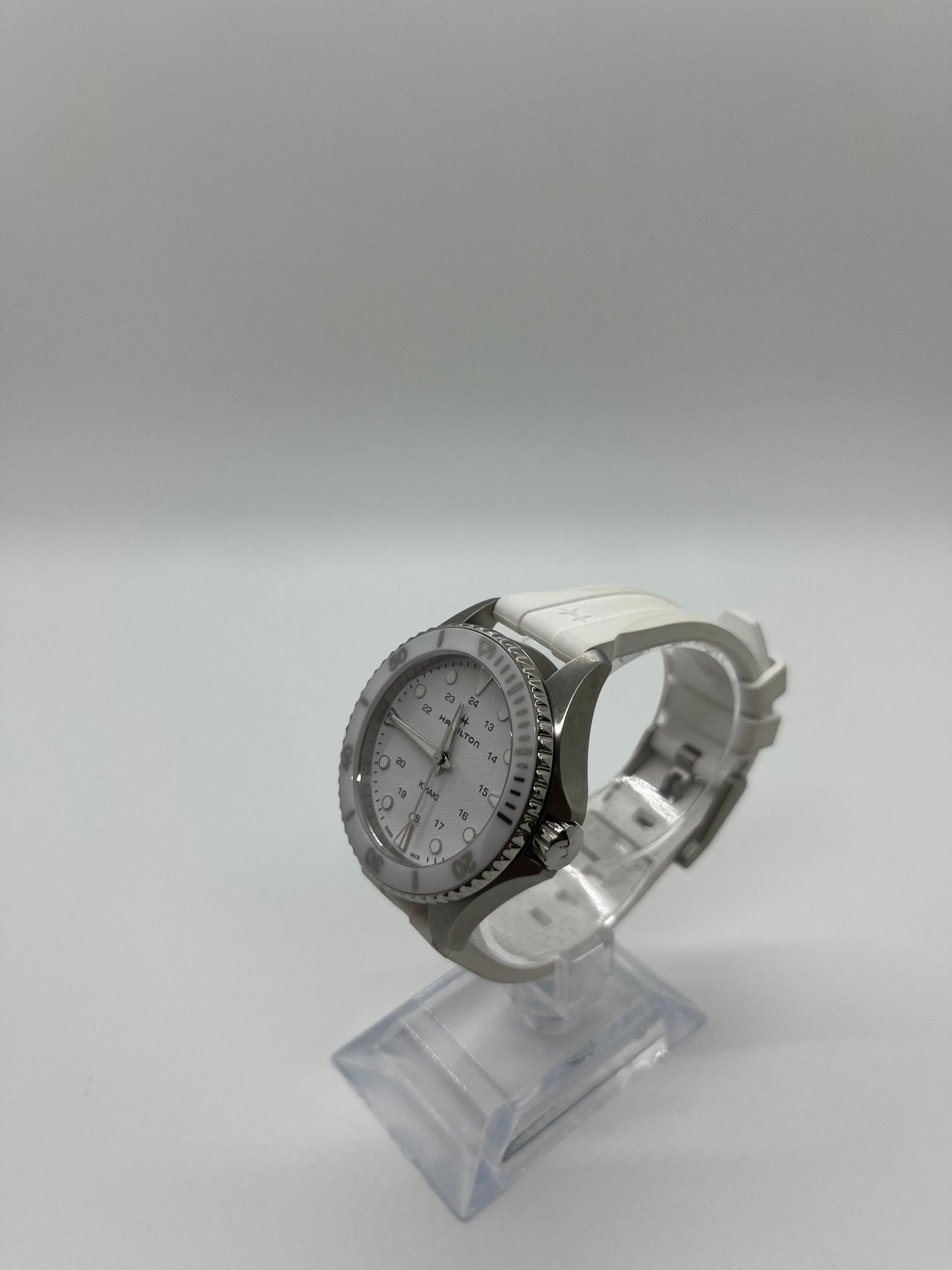 Silver wristwatch with white face and band, displayed on a clear stand.