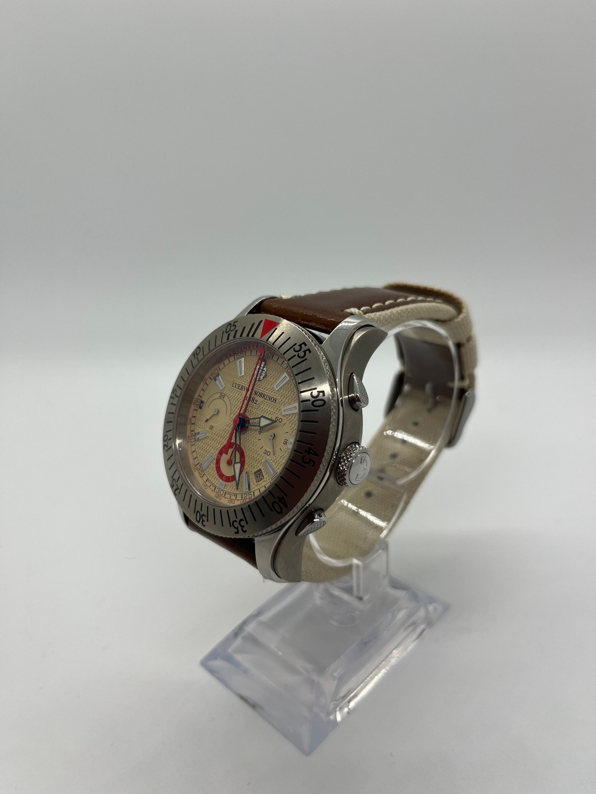 Silver and brown wristwatch on a stand with a beige dial, red accents, and a brown leather band.