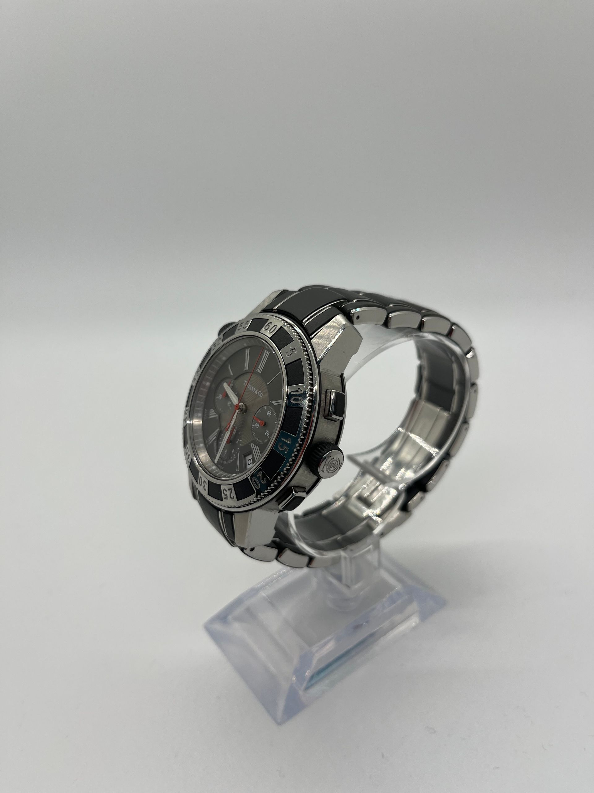 Silver and black wristwatch with red dial on a clear stand against a white background.