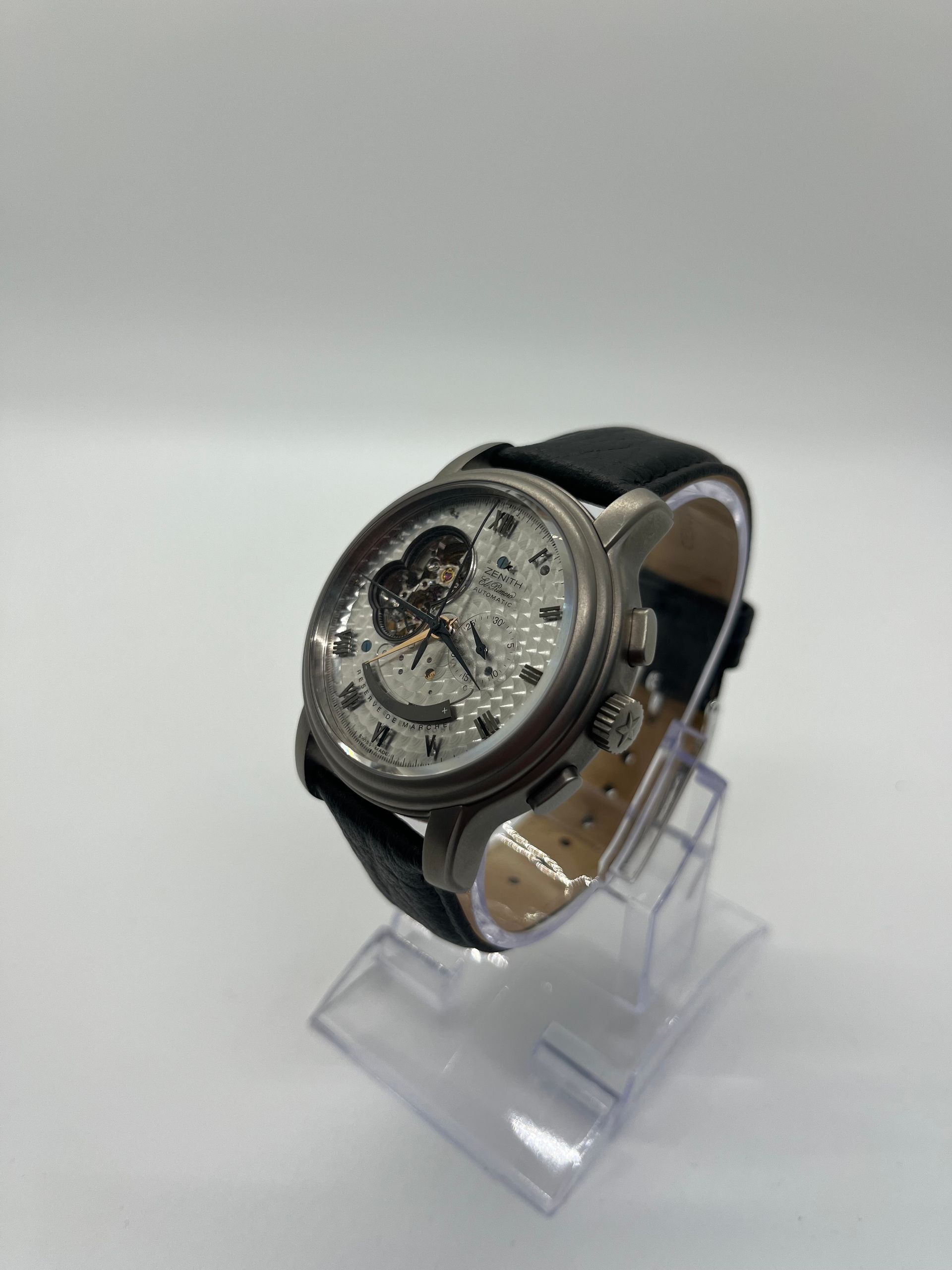 Gray and black Fossil watch with exposed movement on clear display stand.