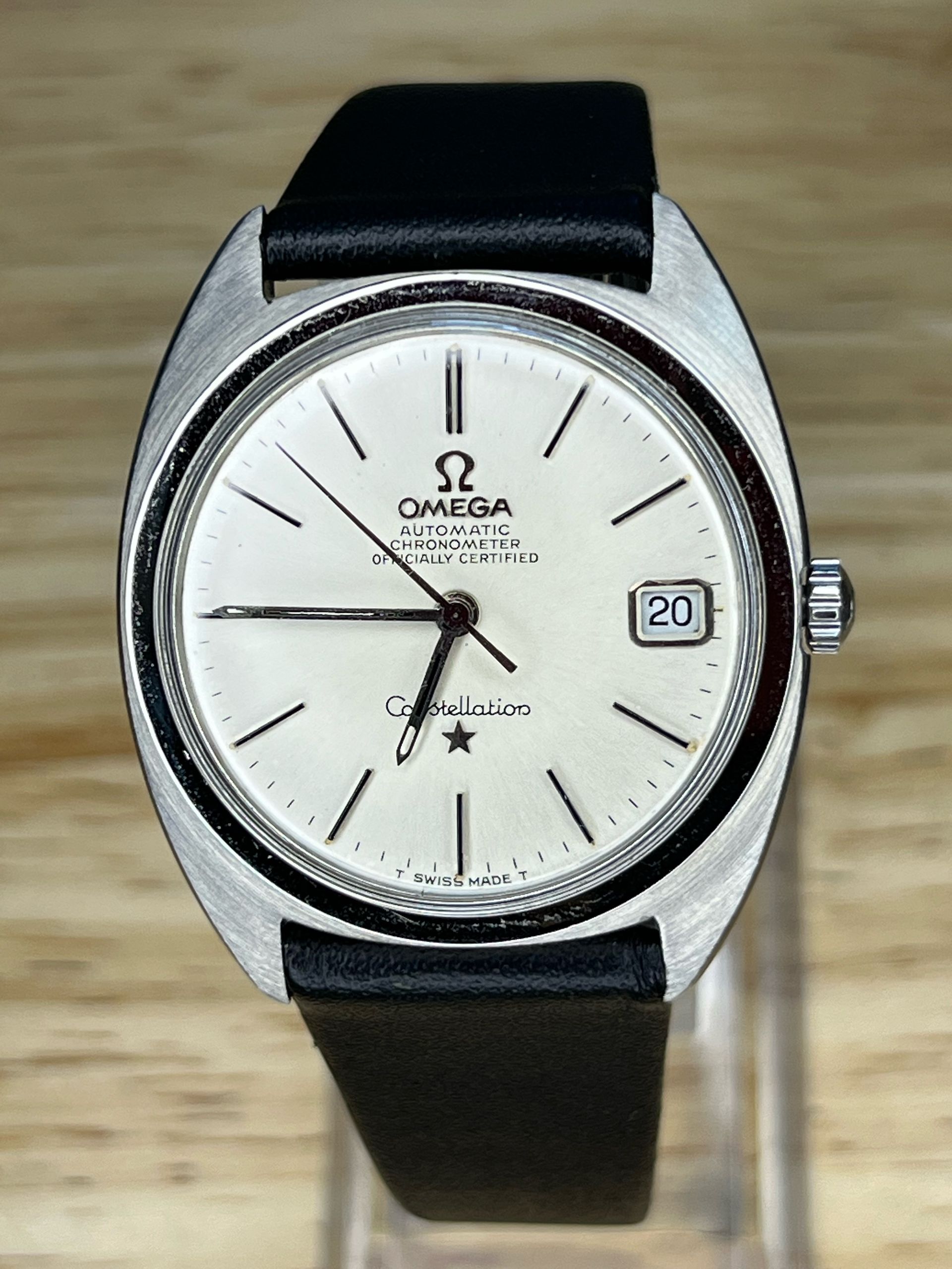 Silver Omega Constellation watch with black leather band and date display.