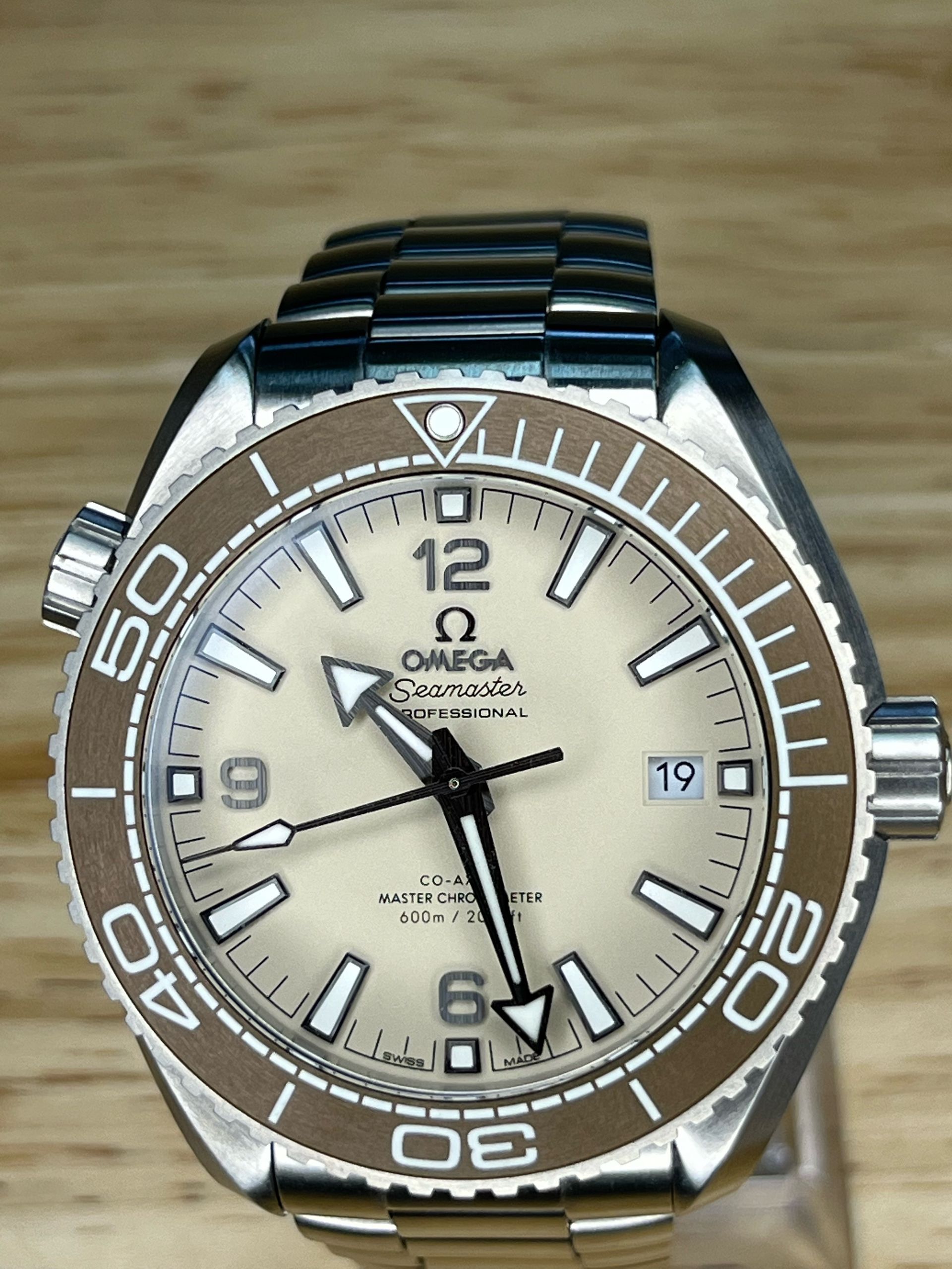 Omega Seamaster watch with tan dial, brown bezel, and stainless steel bracelet.