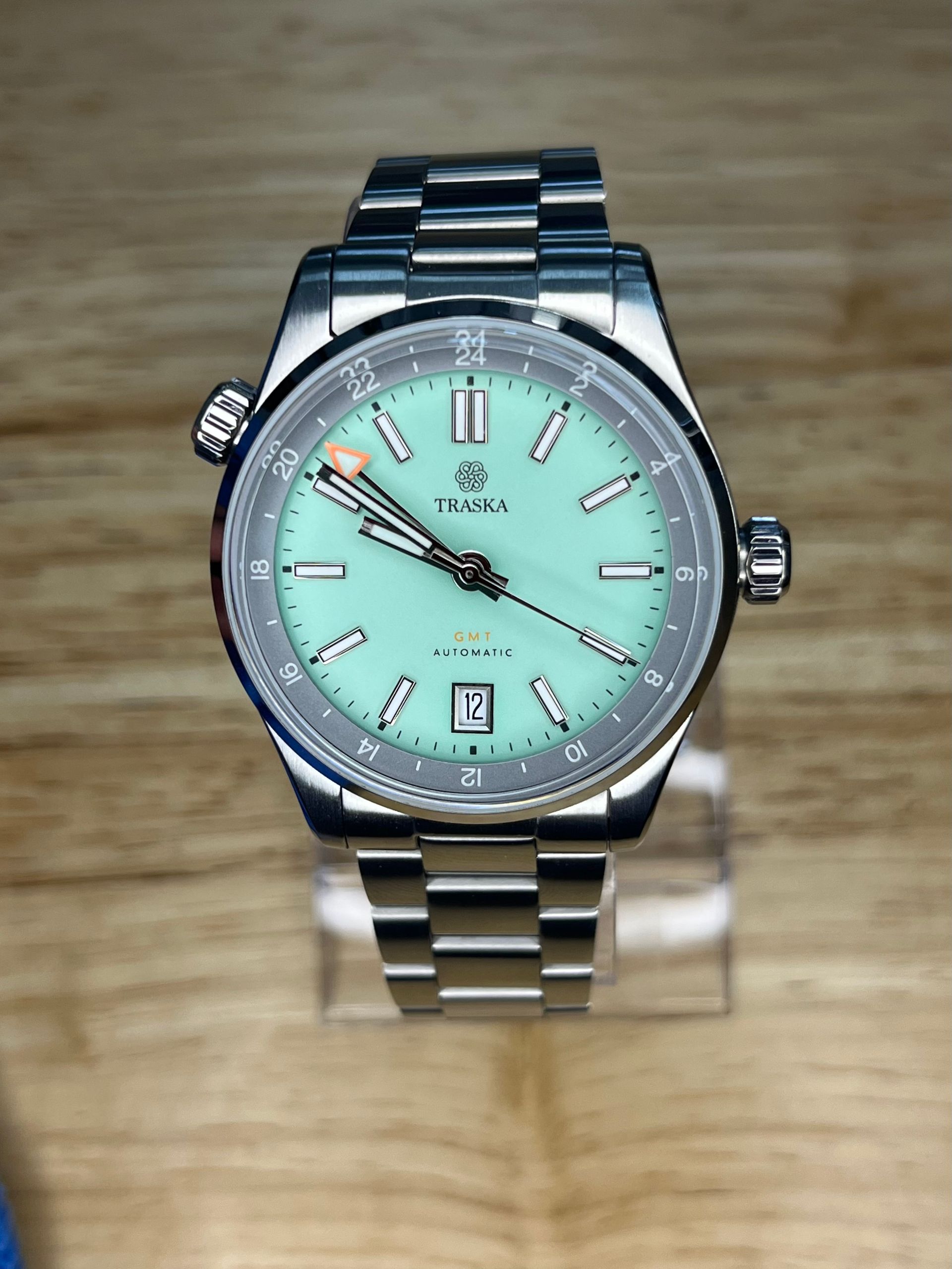 Silver watch with a turquoise face and steel band on a wooden surface.