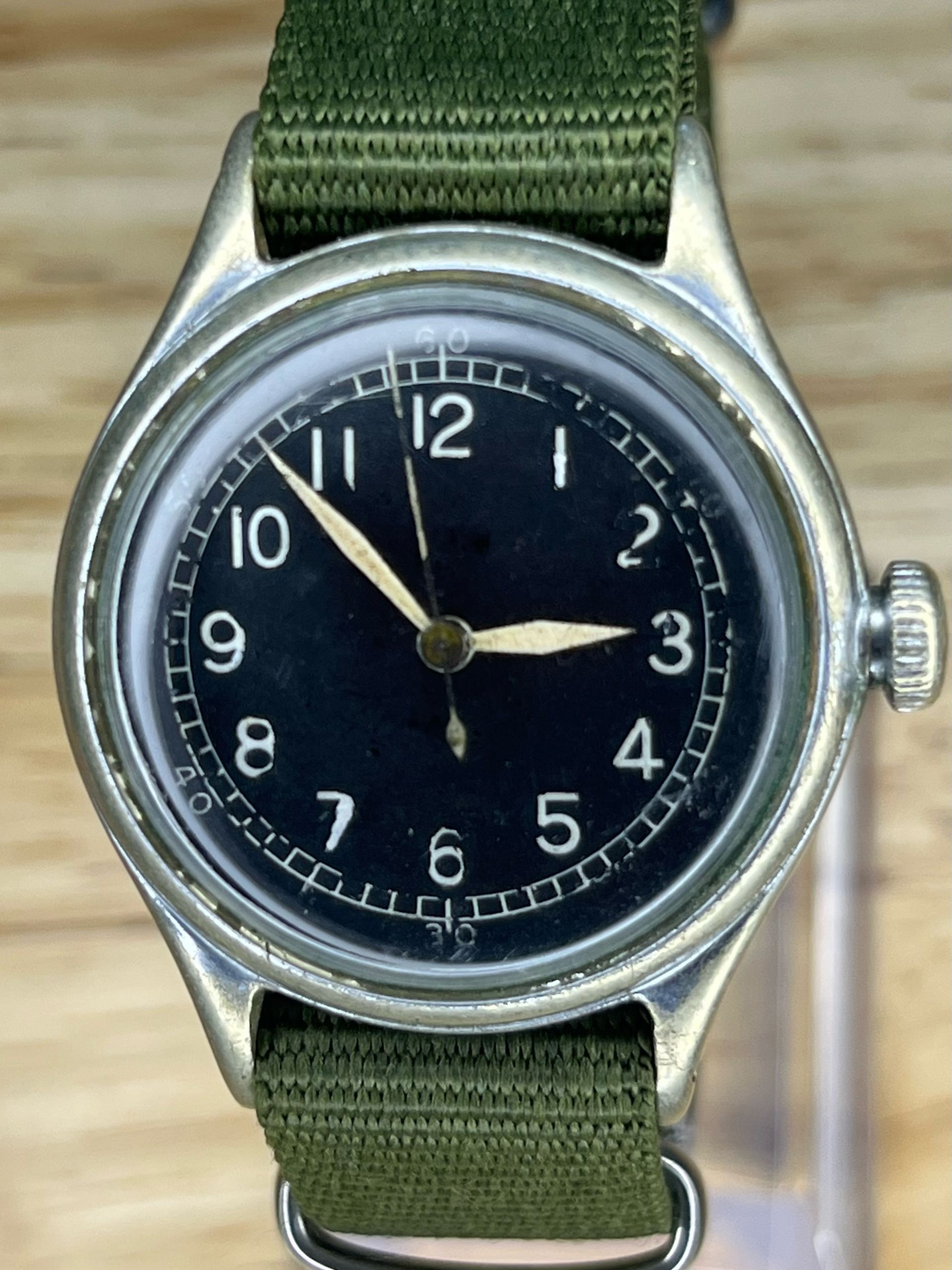 A vintage wristwatch with a black face and a green fabric band.
