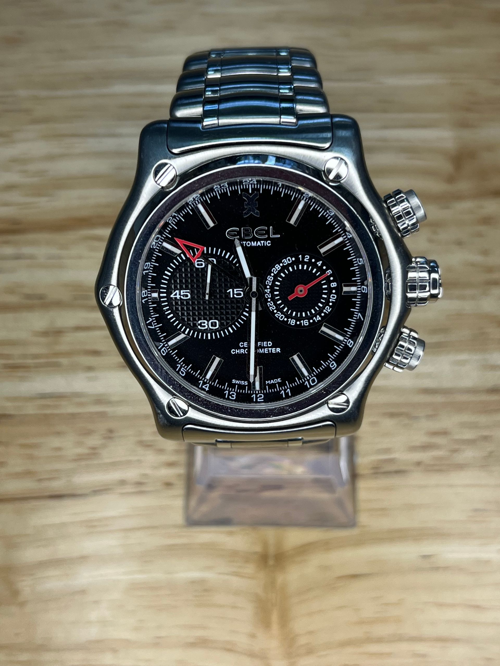 Silver wristwatch with black face and two sub-dials, set on a wooden surface.