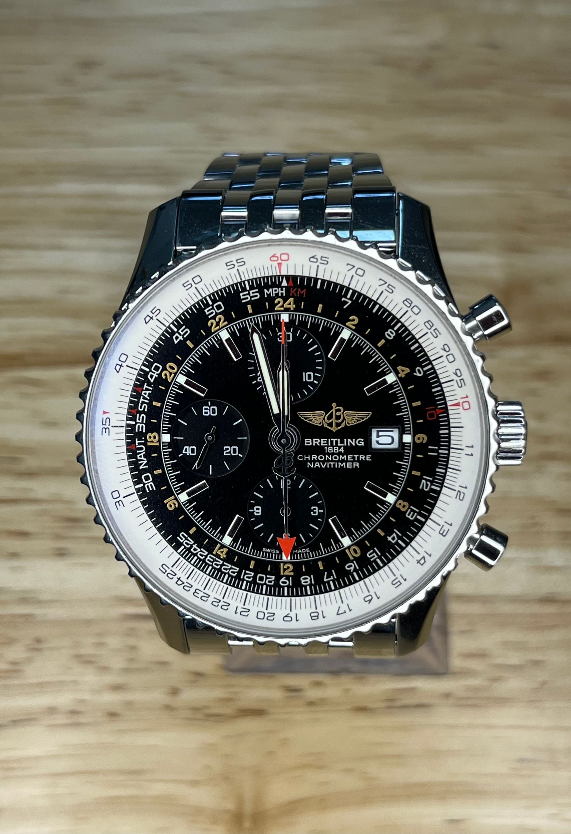 Breitling Navitimer watch with black face, white bezel, silver band, resting on wood surface.