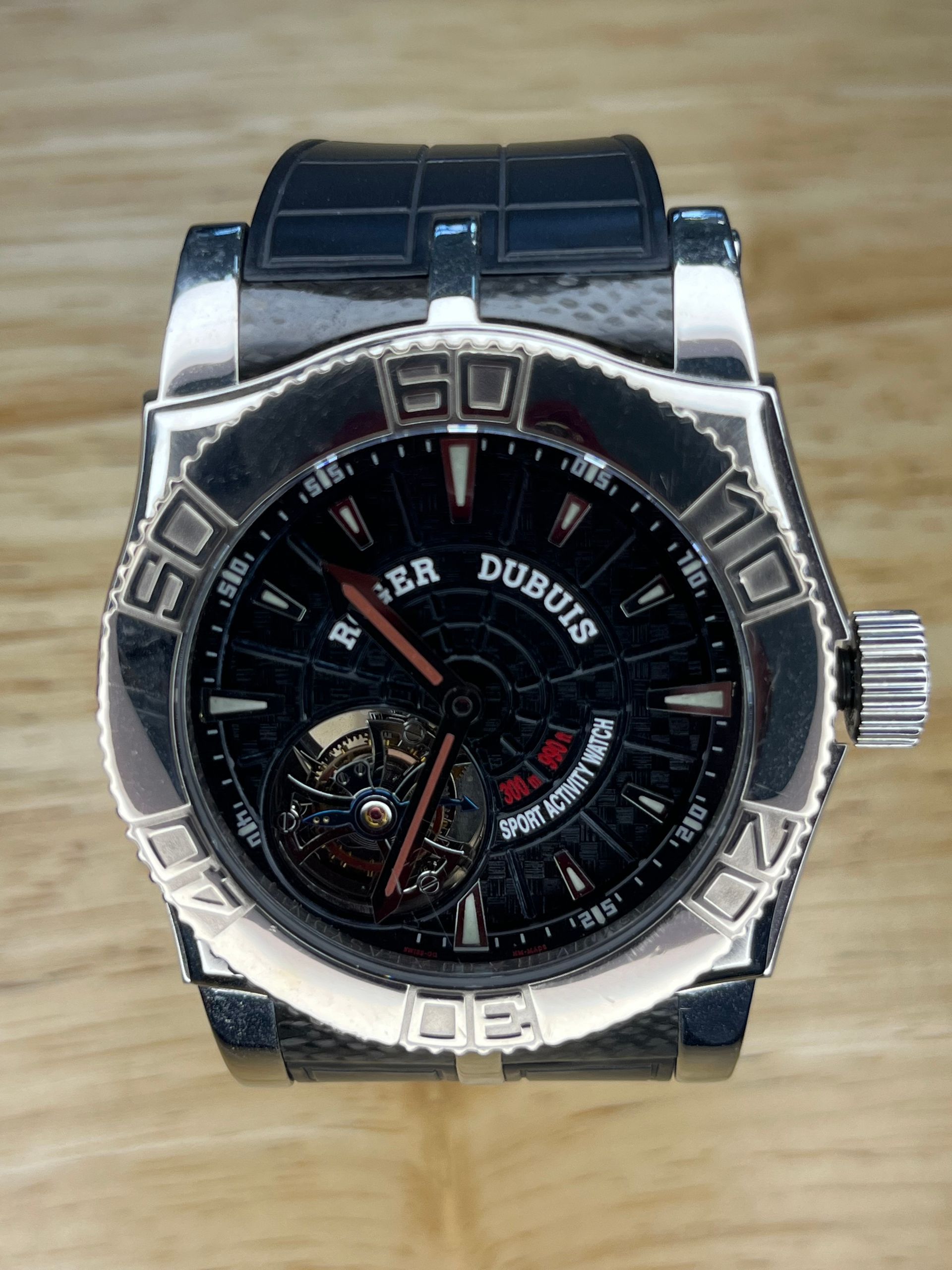 Roger Dubuis black wristwatch with silver bezel on a wooden surface.